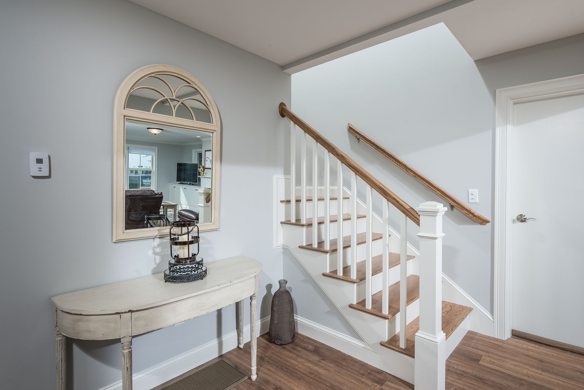 Bright entryway with a white staircase, arched mirror, and small console table on wood floors
