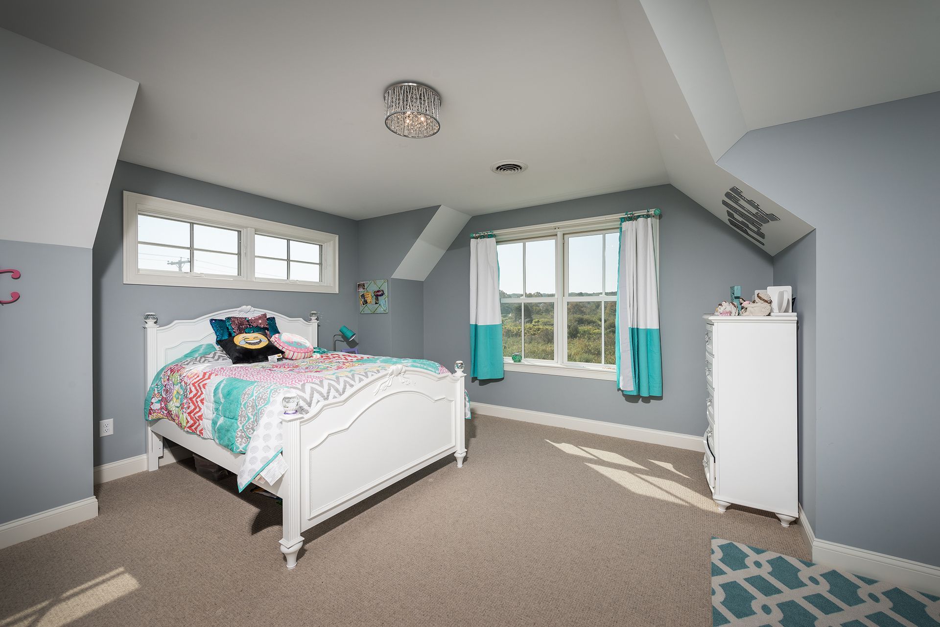 Spacious gray bedroom with white bed, patterned bedding, turquoise curtains, and bright windows.