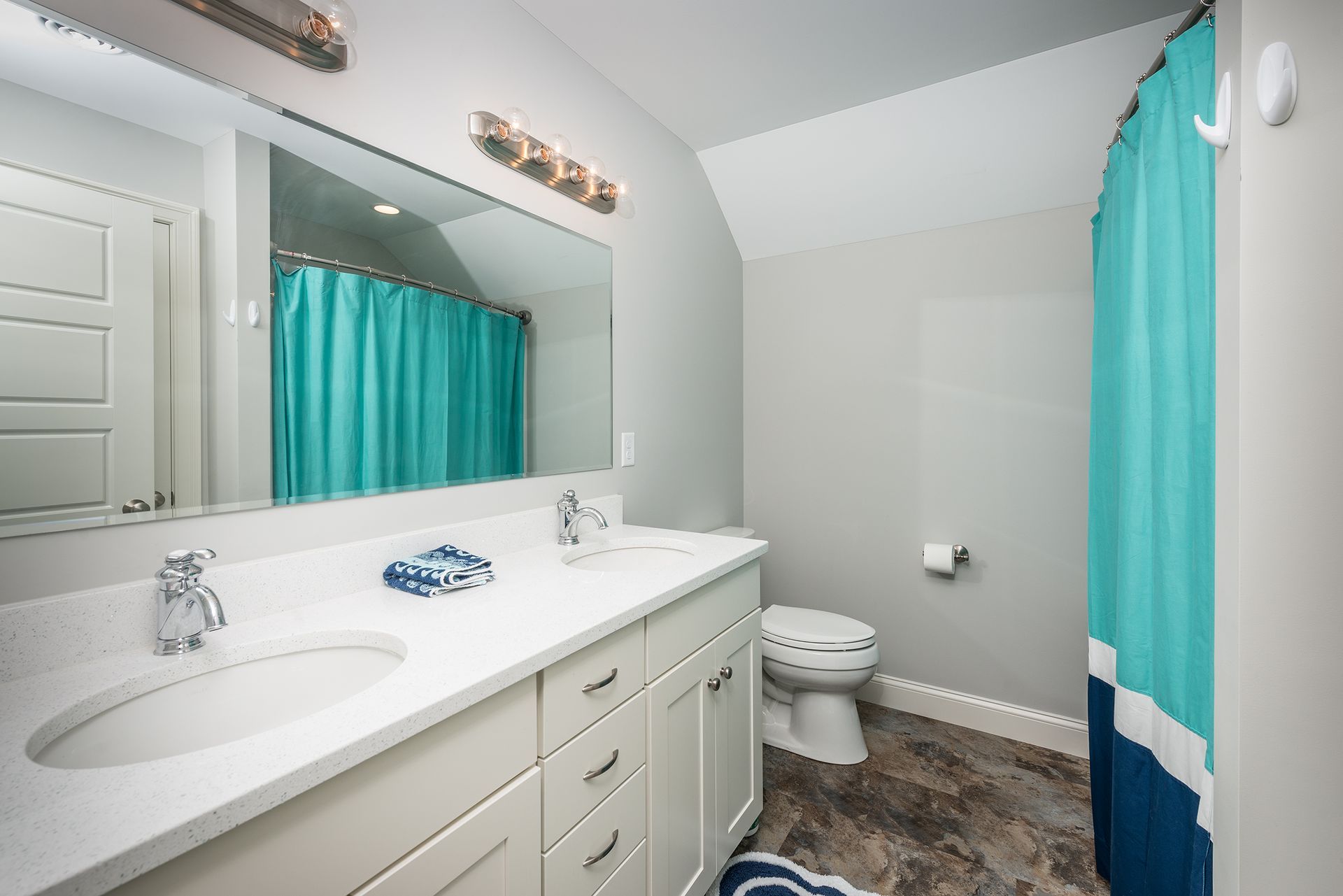 Bright bathroom with double sink vanity, turquoise shower curtain, and toilet