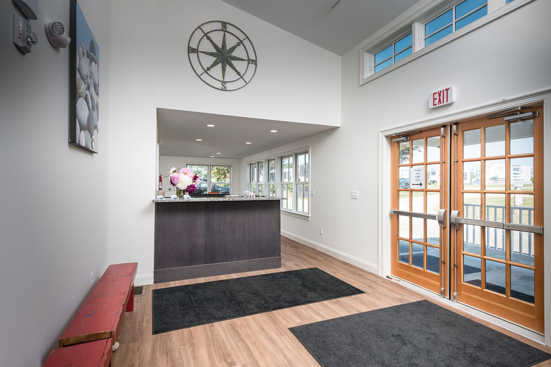 Bright lobby with reception desk, black rugs, wooden floors, and glass double doors