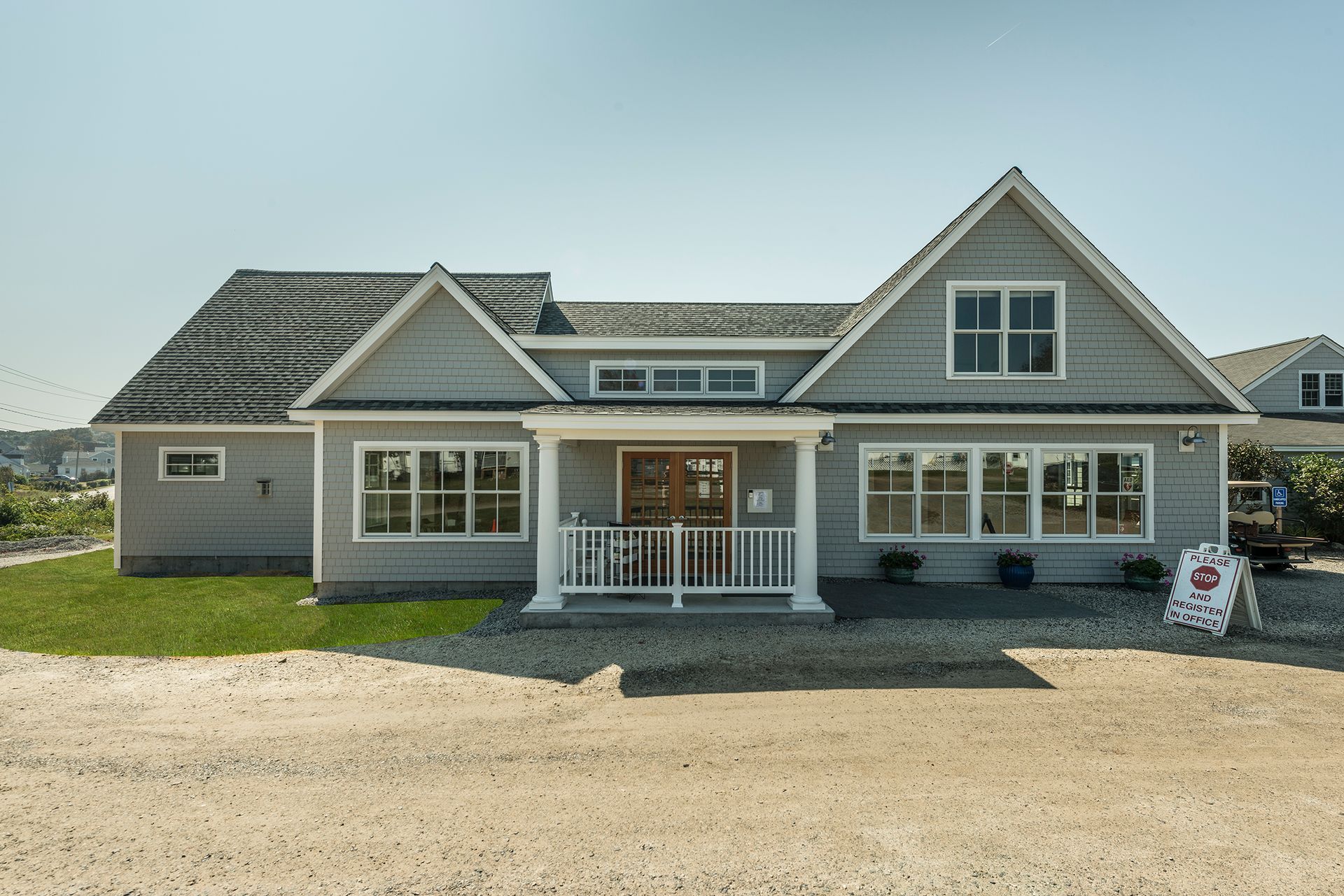 Gray single-story house with white trim and porch, viewed from a gravel driveway under a clear sky