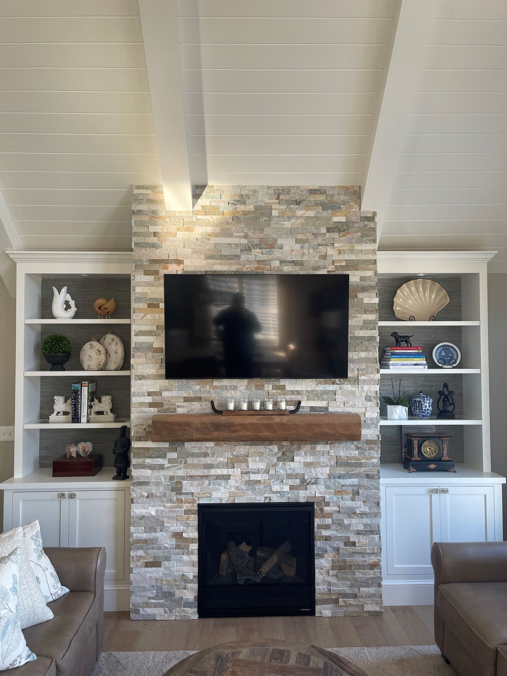 Living room fireplace wall with TV, stone surround, built-in shelves, and vaulted ceiling