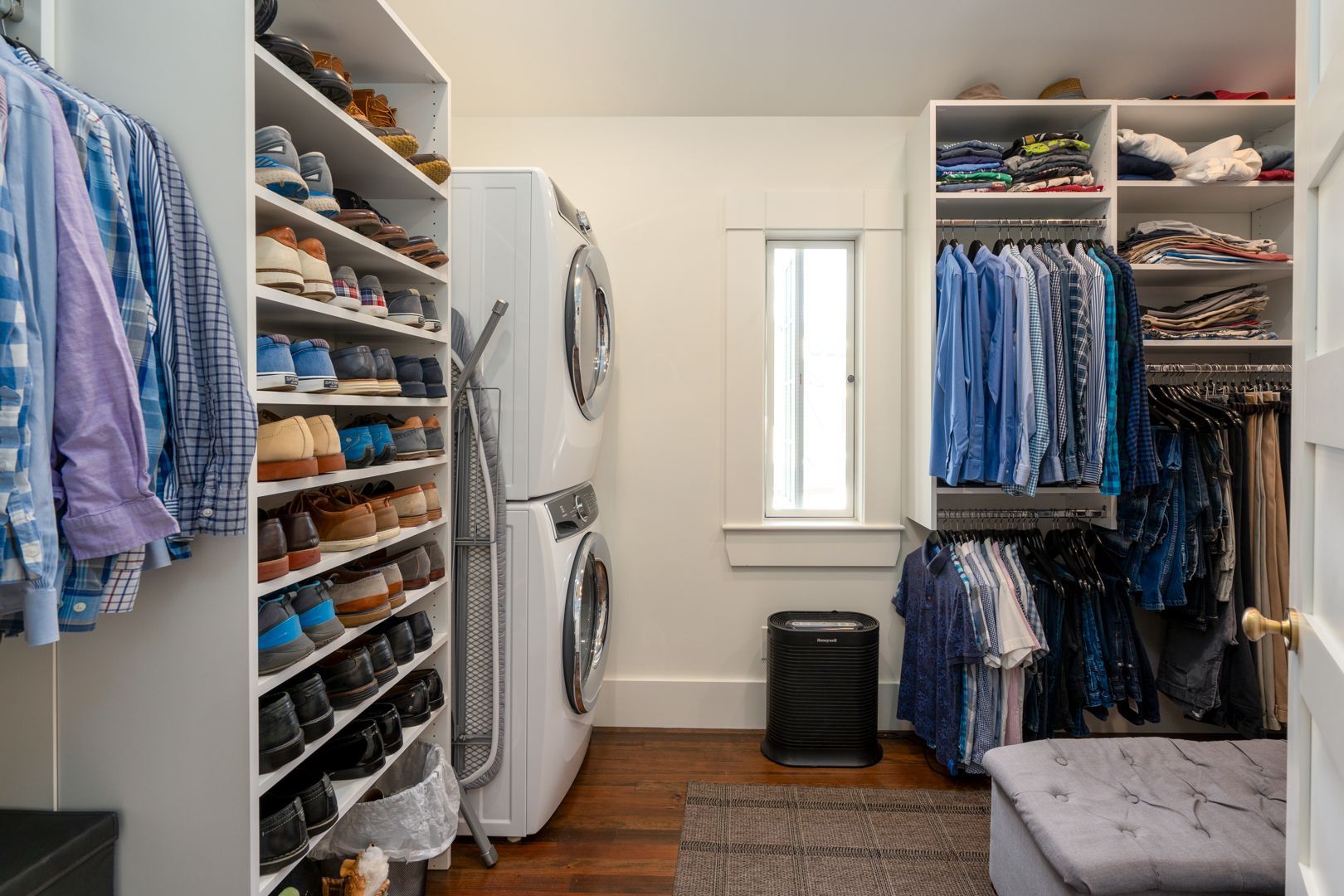 A bright walk-in closet with shelves of folded clothes, hanging garments, and stacked washer and dryer.