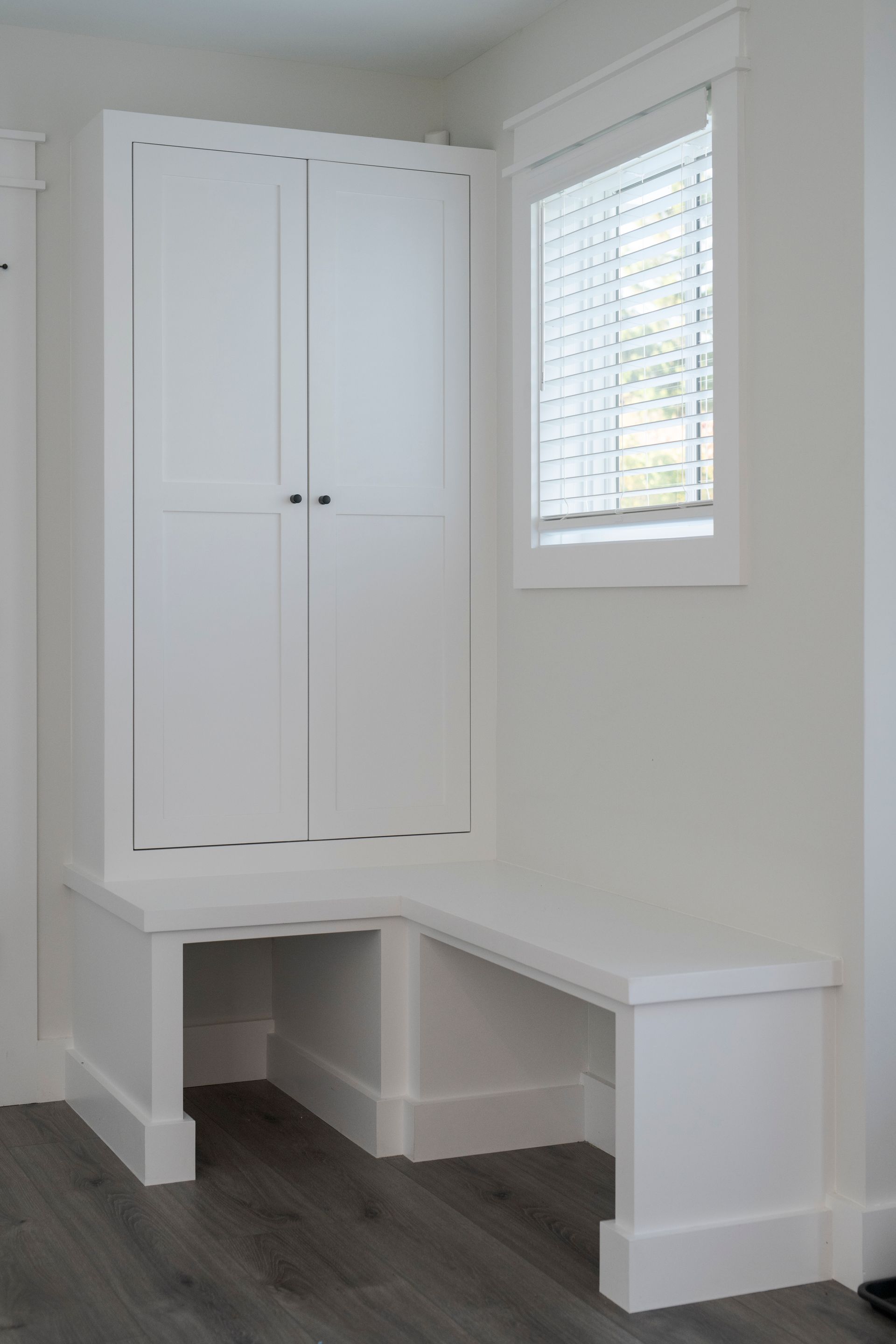 Built-in white desk nook with cabinet storage beside a window in a bright room