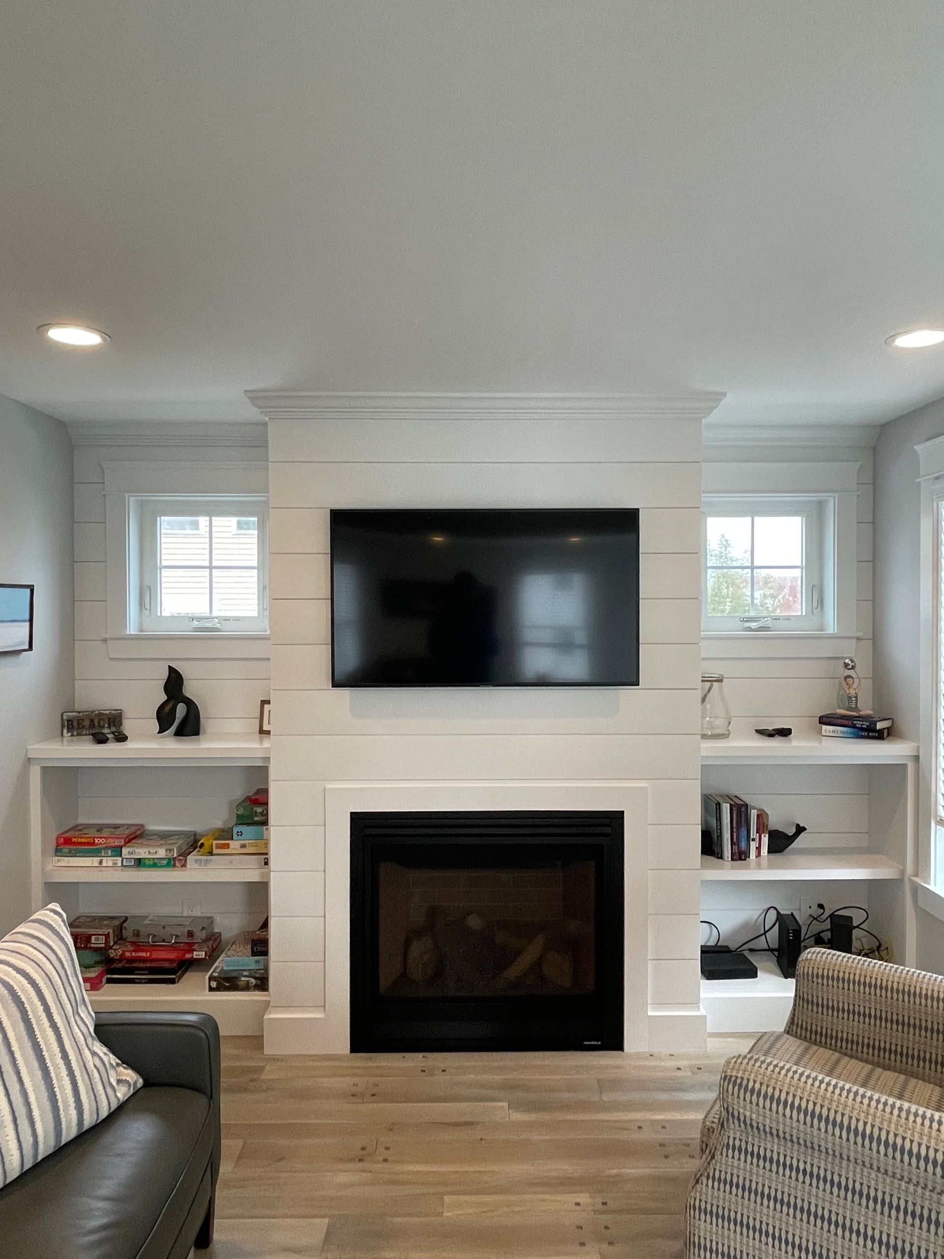 Bright living room with a mounted TV above a fireplace, built-in shelves, and light wood floors