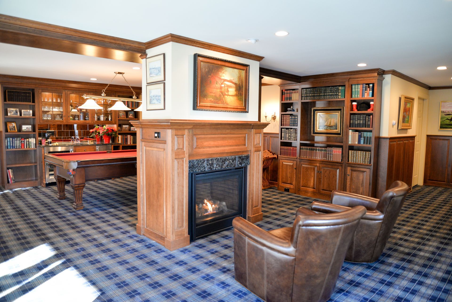 Cozy library lounge with fireplace, leather chairs, blue carpet, and wood-paneled bookshelves