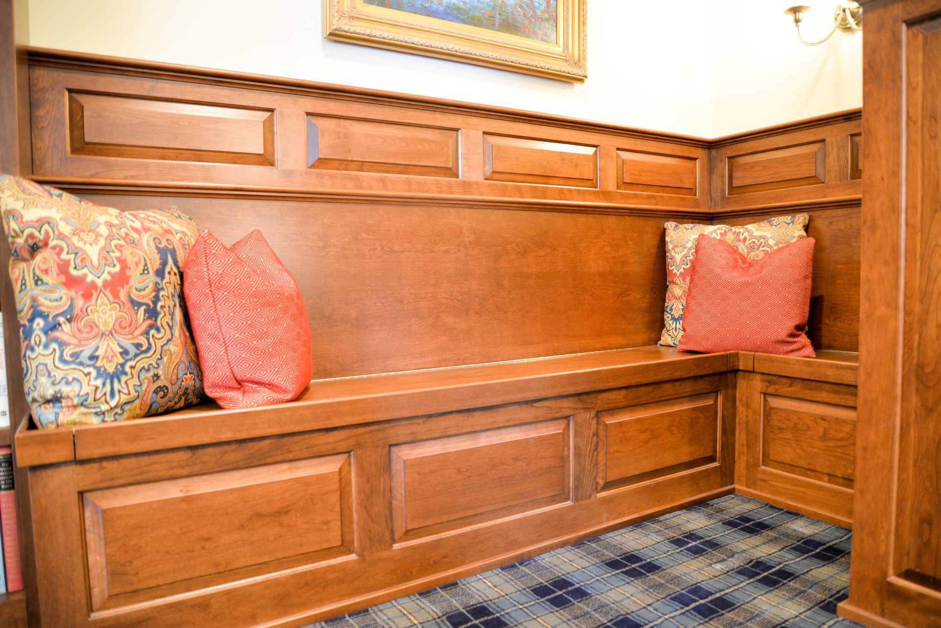 Wood-paneled window seat with coral and patterned cushions in a cozy room