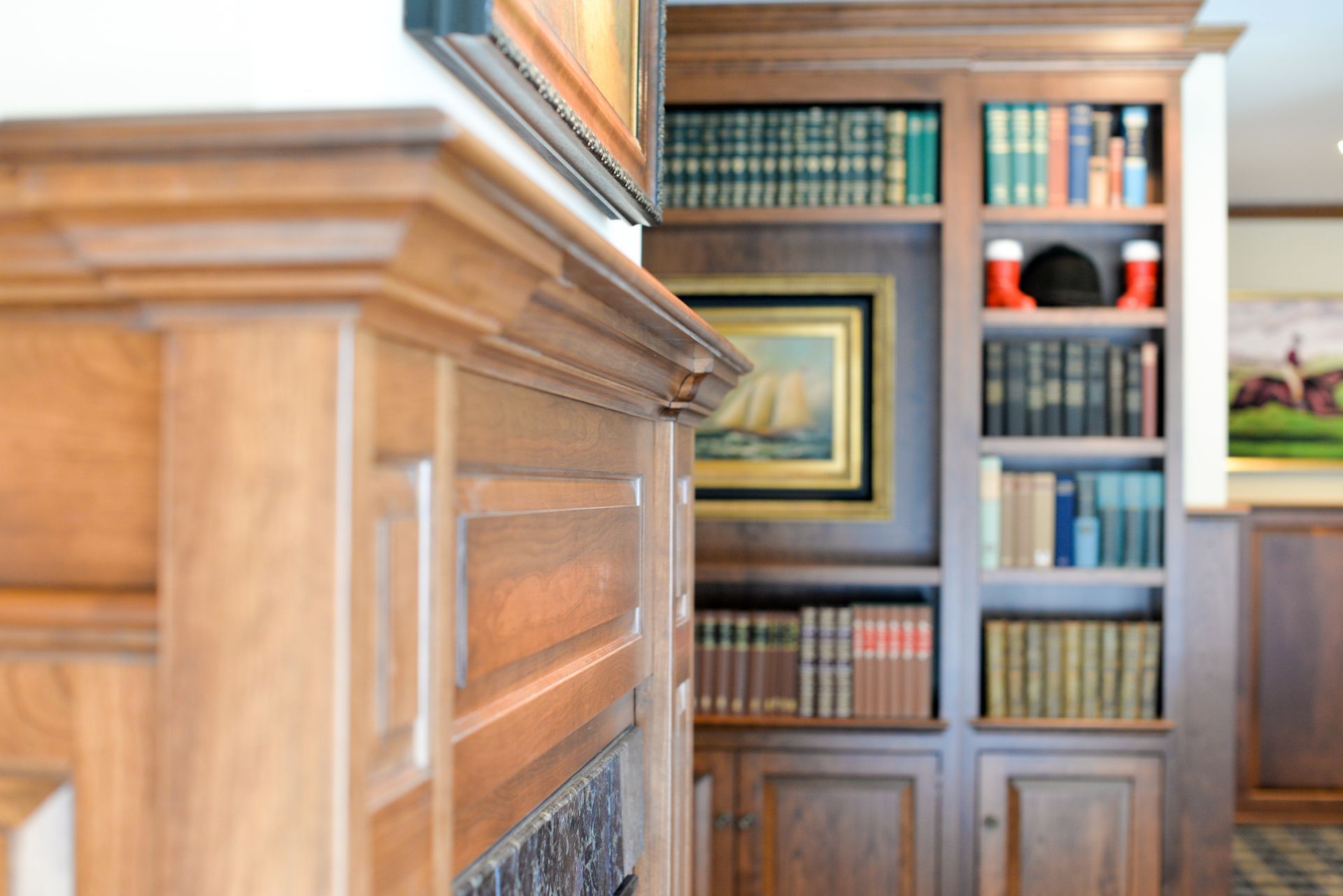 Wood-paneled library with built-in bookshelves, a framed painting, and a fireplace mantel in the foreground