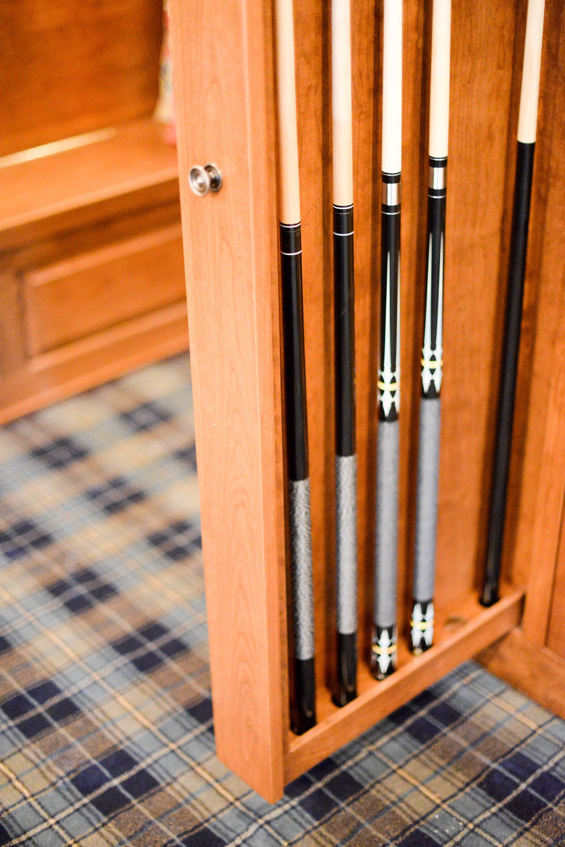 Wooden pool cue rack with several cue sticks standing on a plaid carpet.
