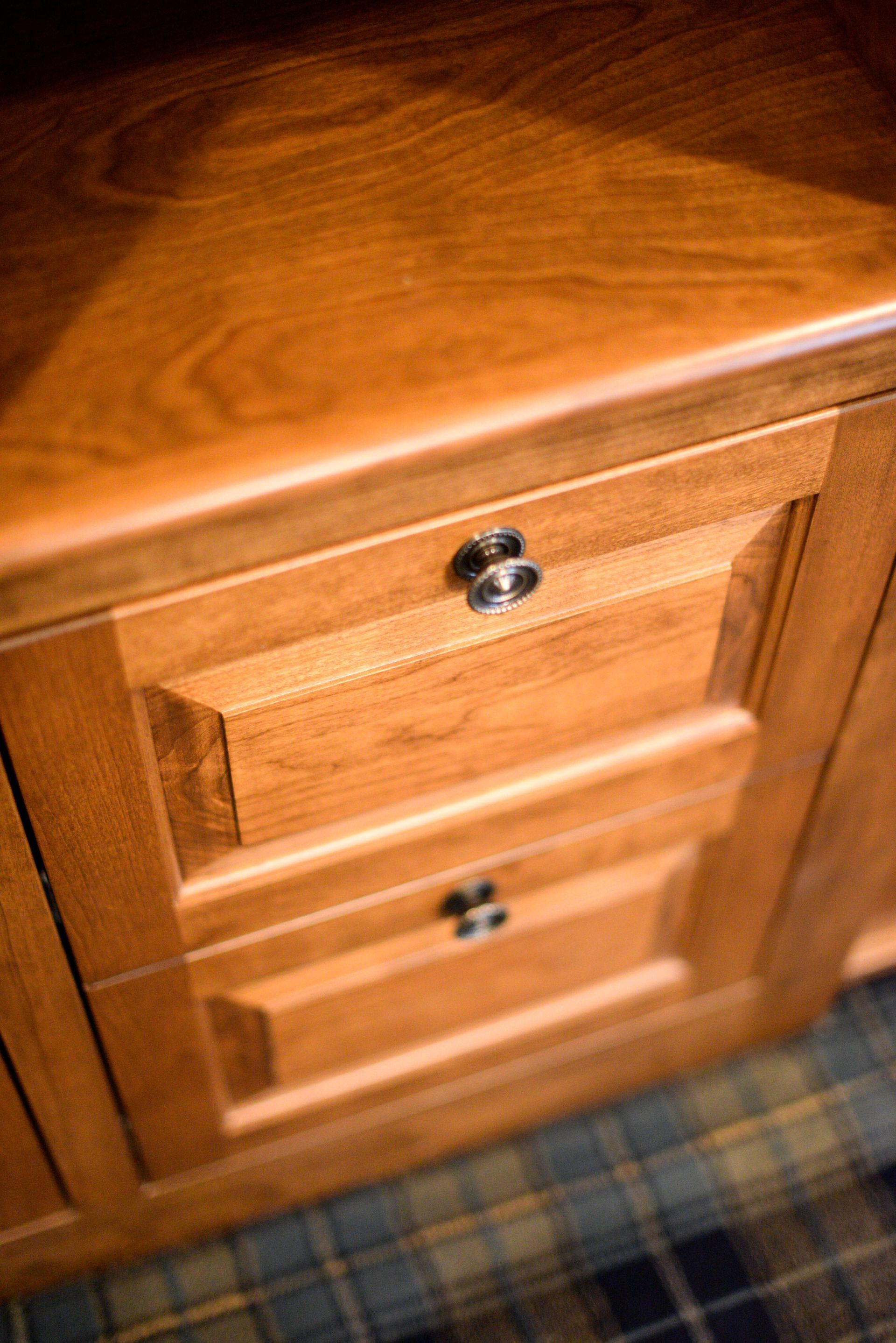 Close-up of a wooden dresser with two drawers and metal knobs on a plaid carpet.