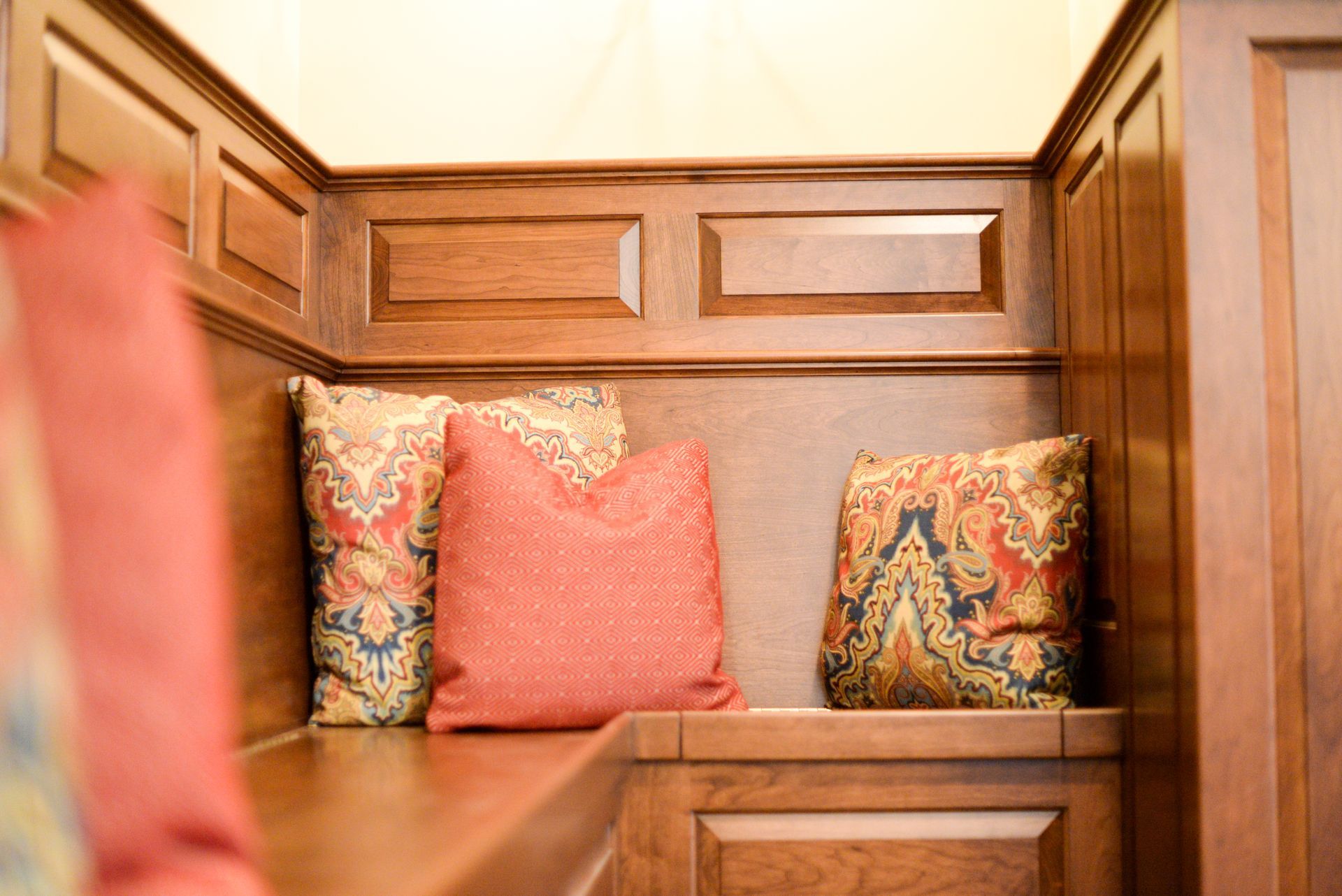 Wooden bench nook with coral and patterned cushions in a warm-toned room