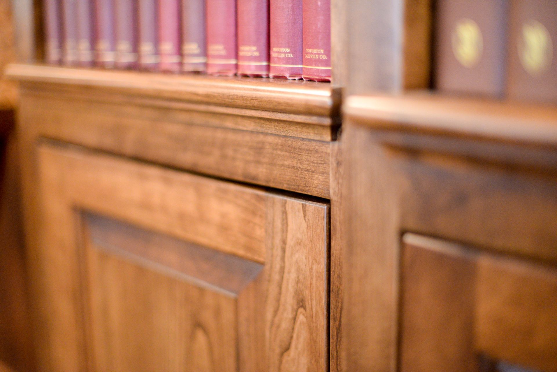 Close-up of wooden bookshelves with red and brown books on the top shelf