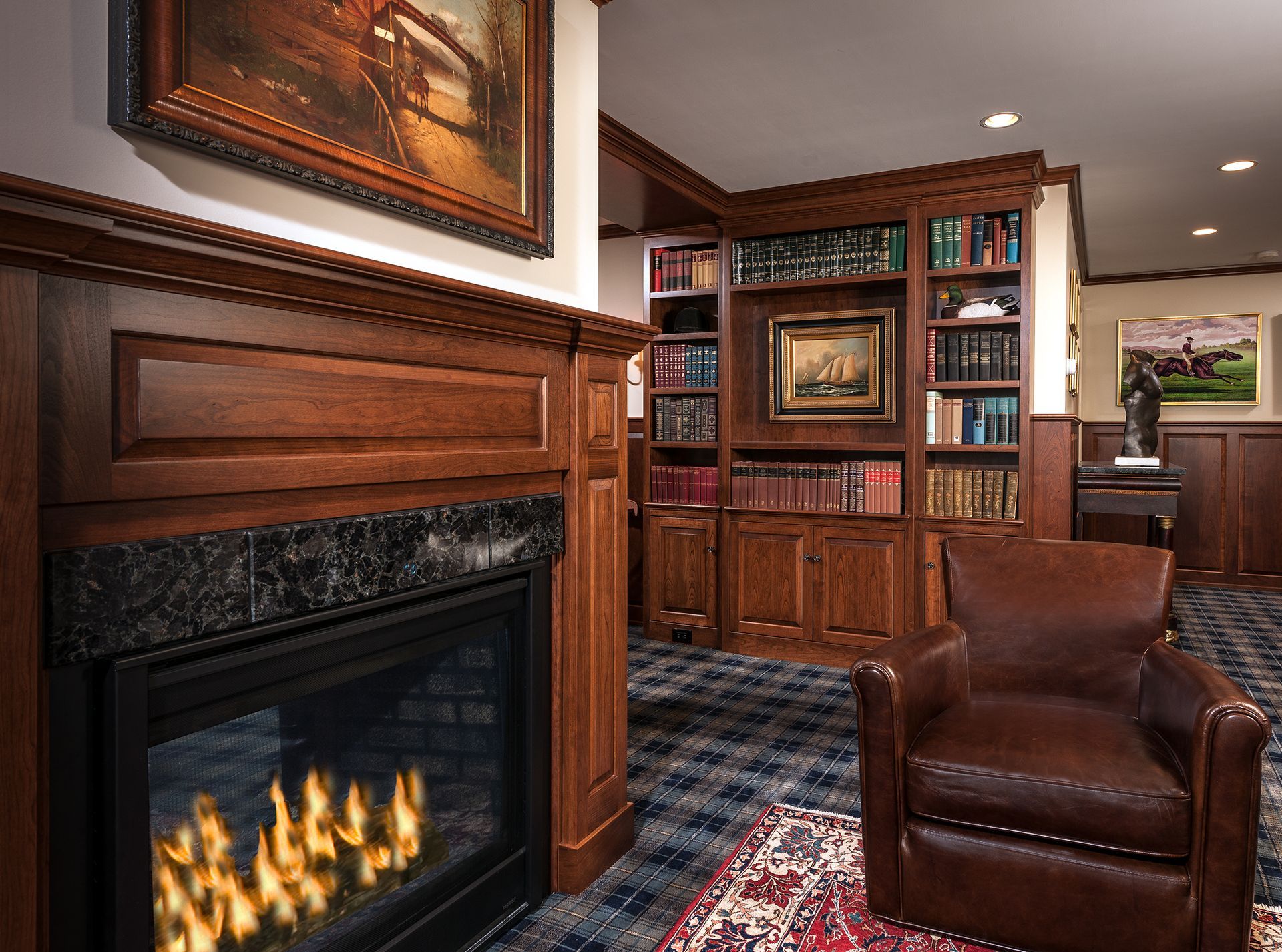 Cozy wood-paneled study with fireplace, leather chair, bookshelves, and red patterned rug
