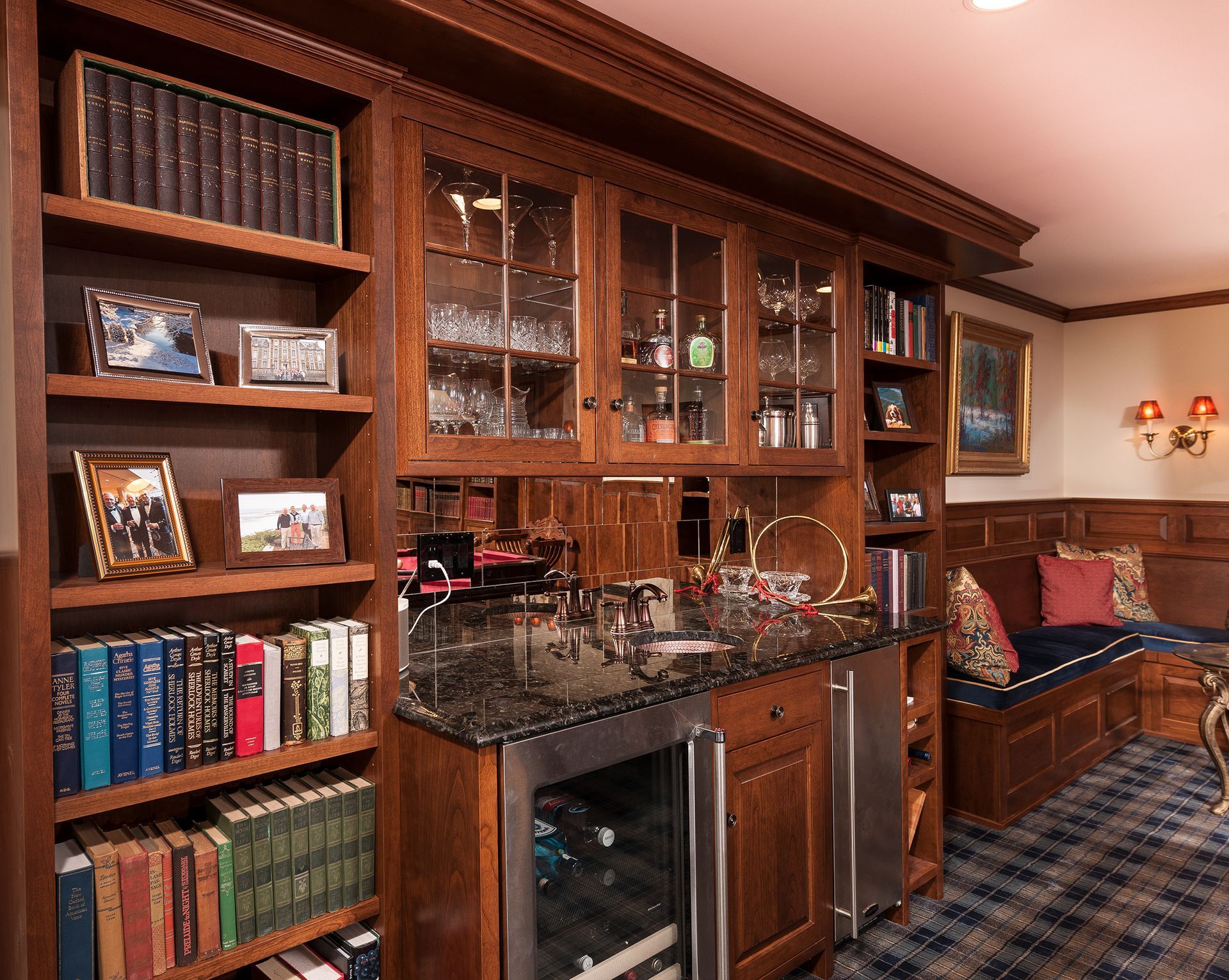 Wood-paneled home bar with built-in shelves, glass cabinets, granite counter, and plaid seating area