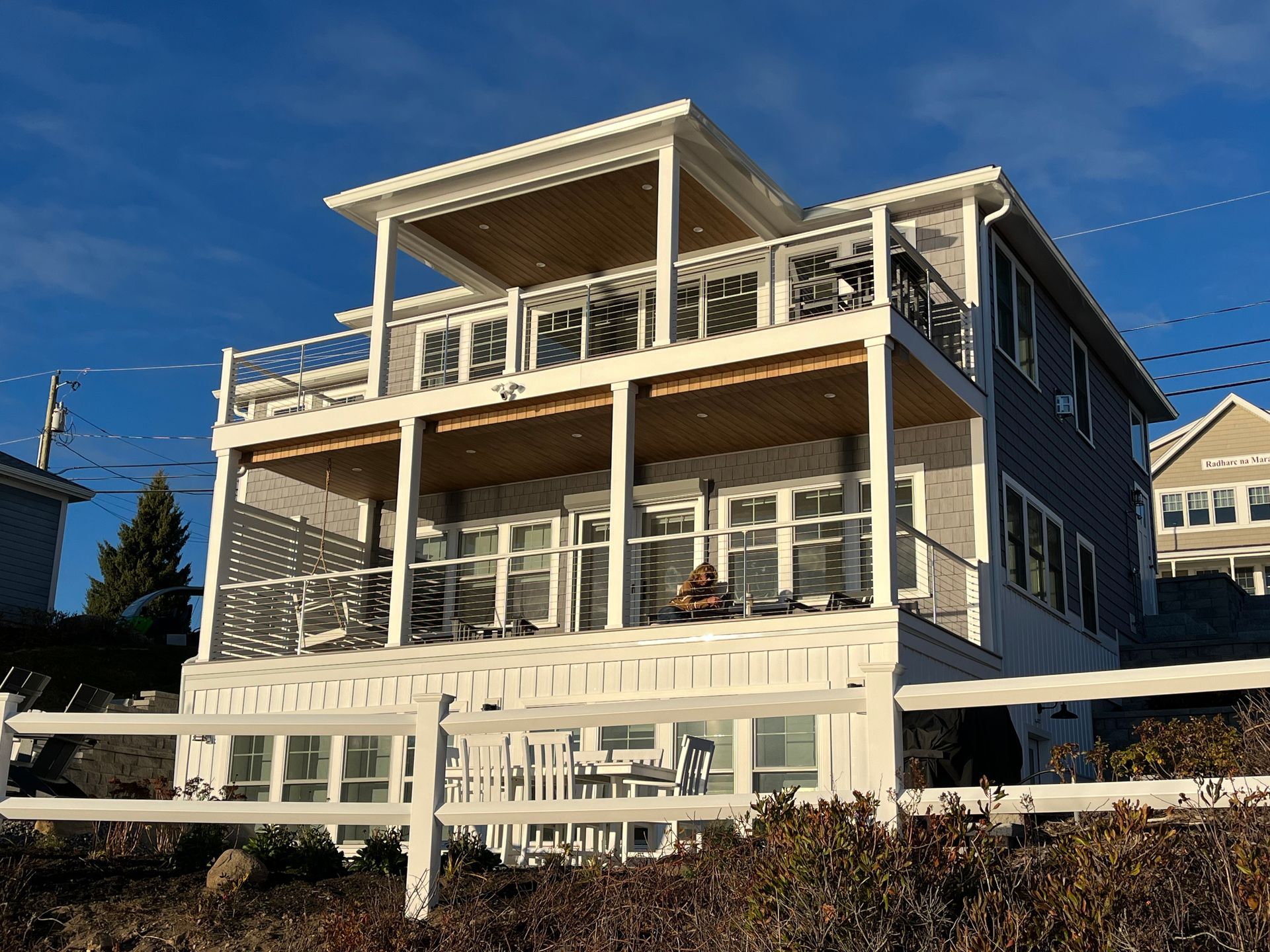 White two-story house with large porches and a rooftop deck under a clear blue sky