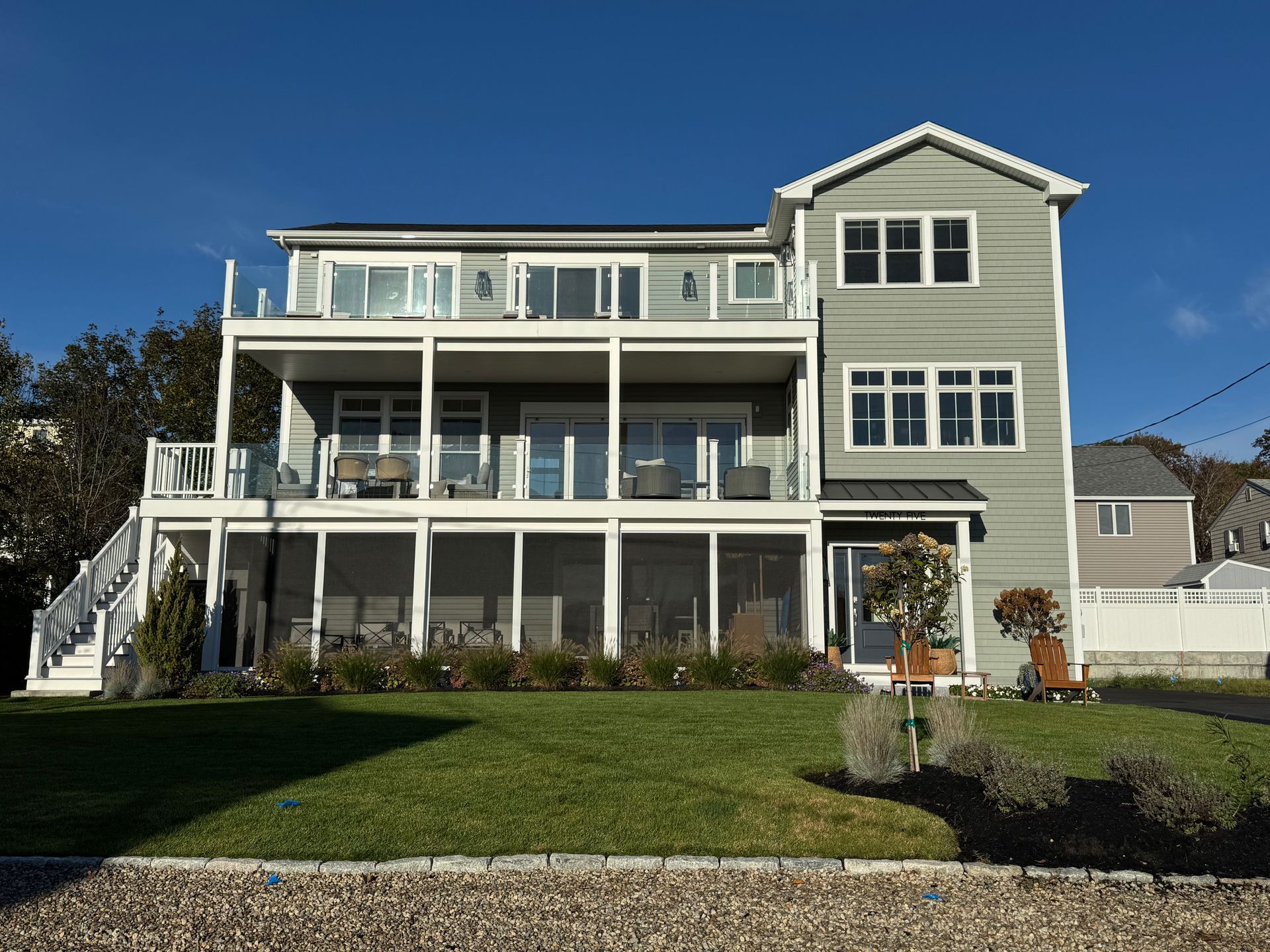 Large pale green house with white trim, wraparound porches, and a manicured front lawn under a blue sky