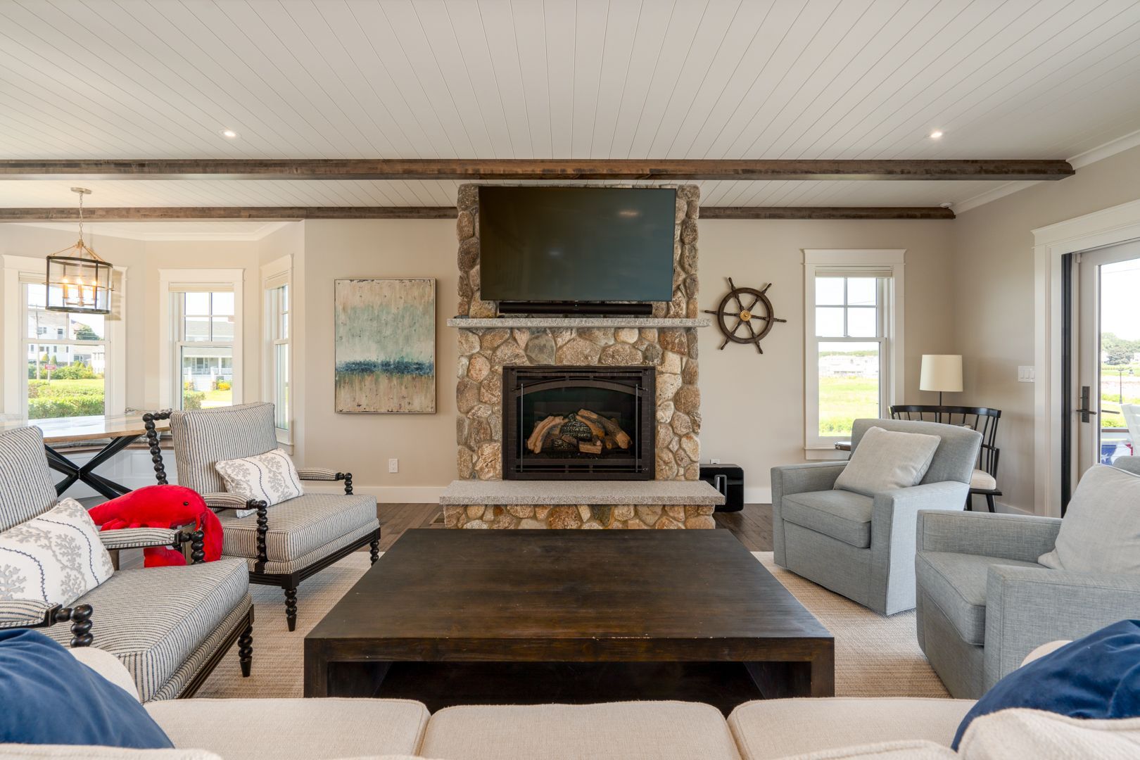Bright living room with a stone fireplace, wall-mounted TV, gray sofas, and a dark wooden coffee table.