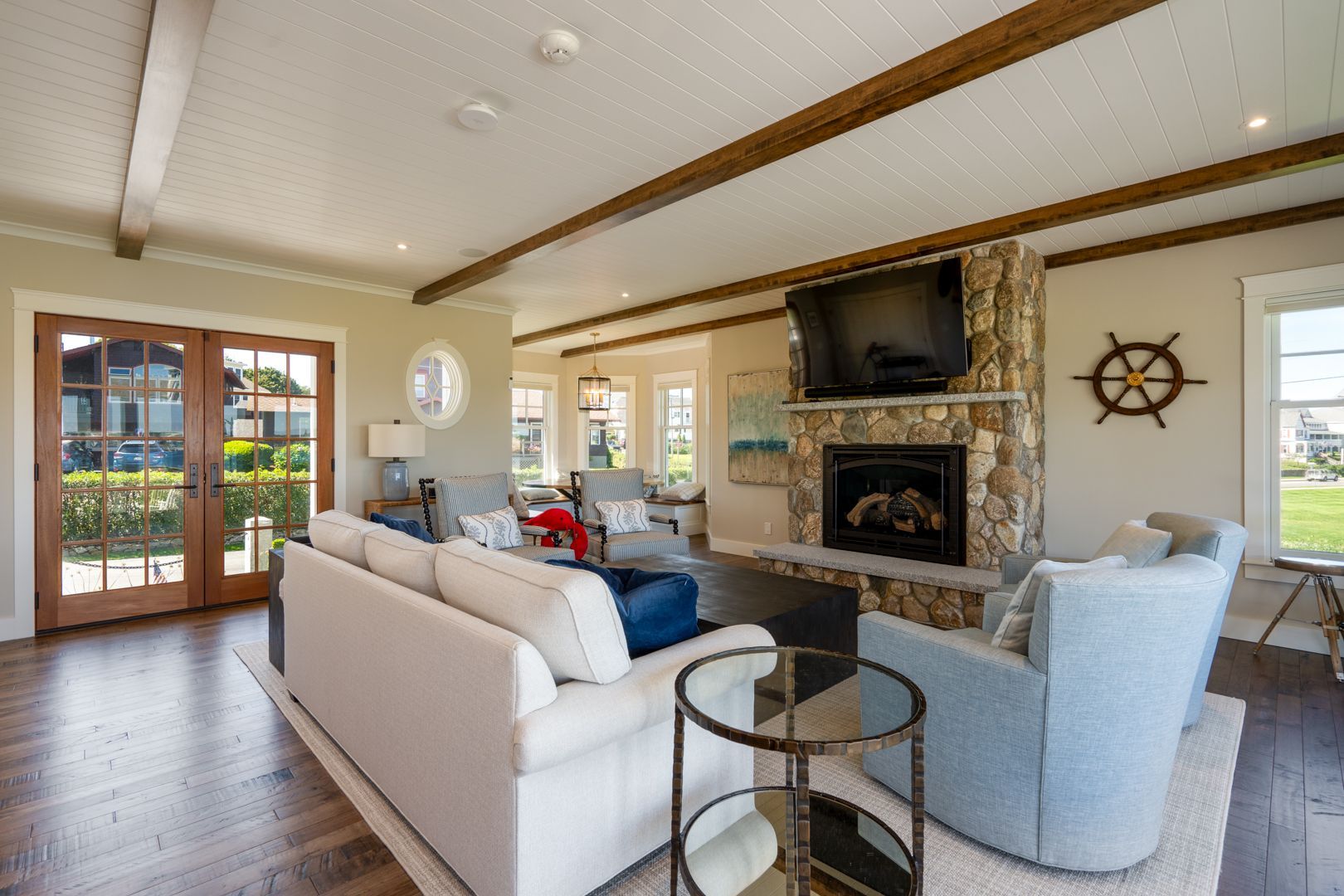 Bright living room with sofas, stone fireplace, TV, and wood-beam ceiling.