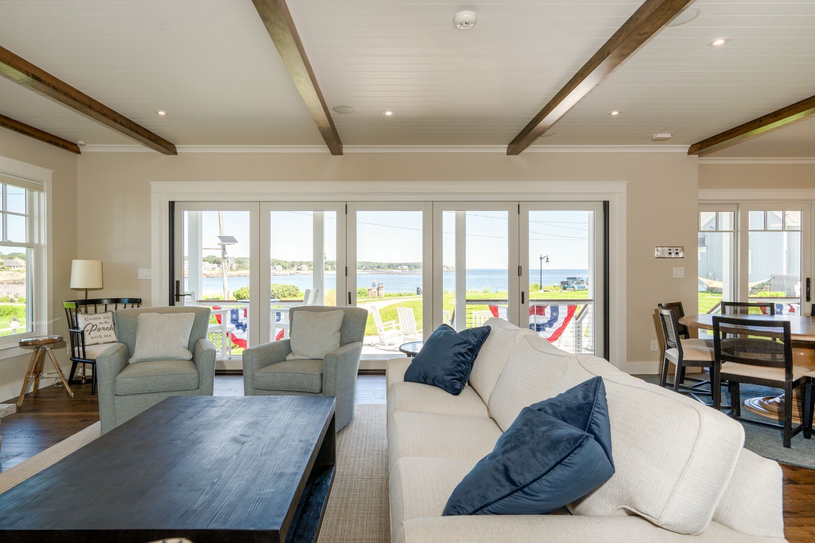 Bright living room with white sofa, blue pillows, dark coffee table, and ocean view through large windows