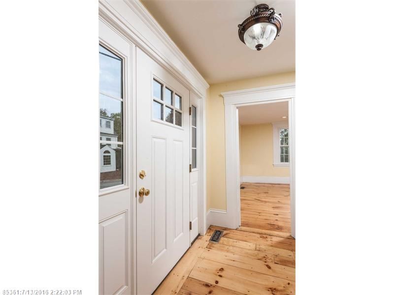 Bright hallway with white doors, wood floors, and a ceiling light, leading to another room