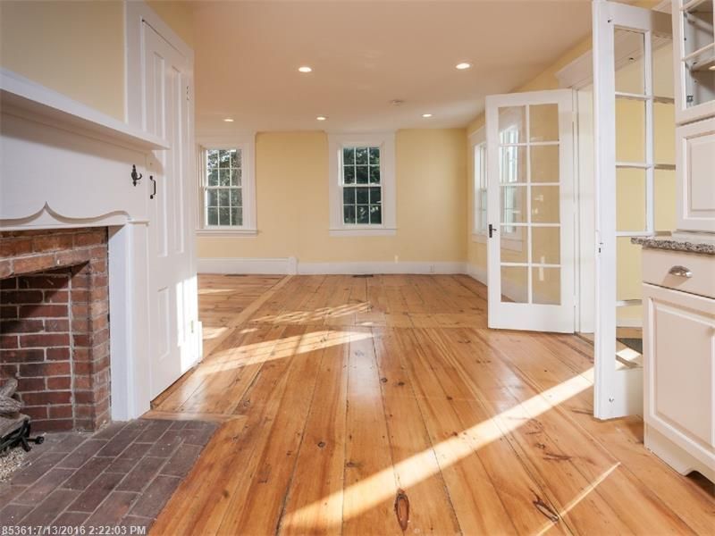 Bright empty living room with hardwood floors, fireplace, and French doors opening to a sunlit space