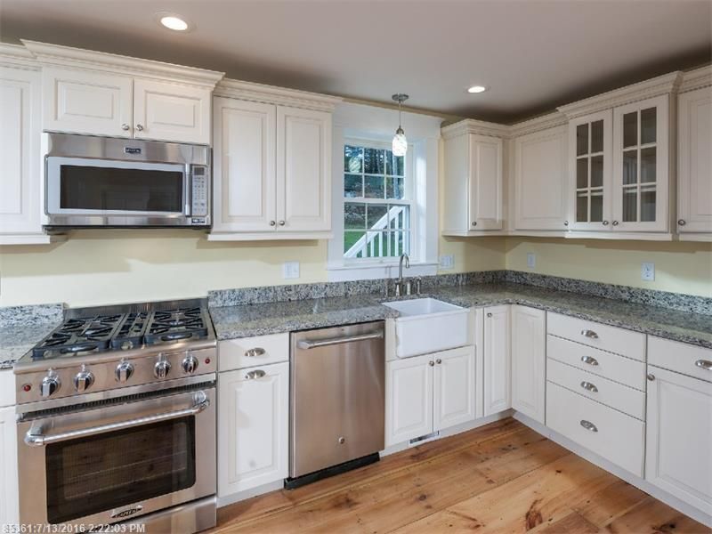 Bright white kitchen with stainless steel appliances, granite counters, and wood floor