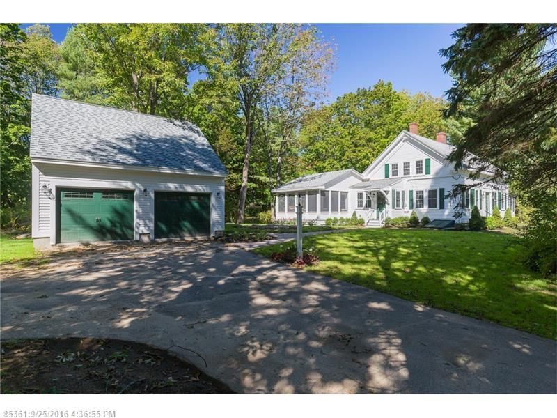 White house with green garage and large lawn beside a driveway under sunny trees
