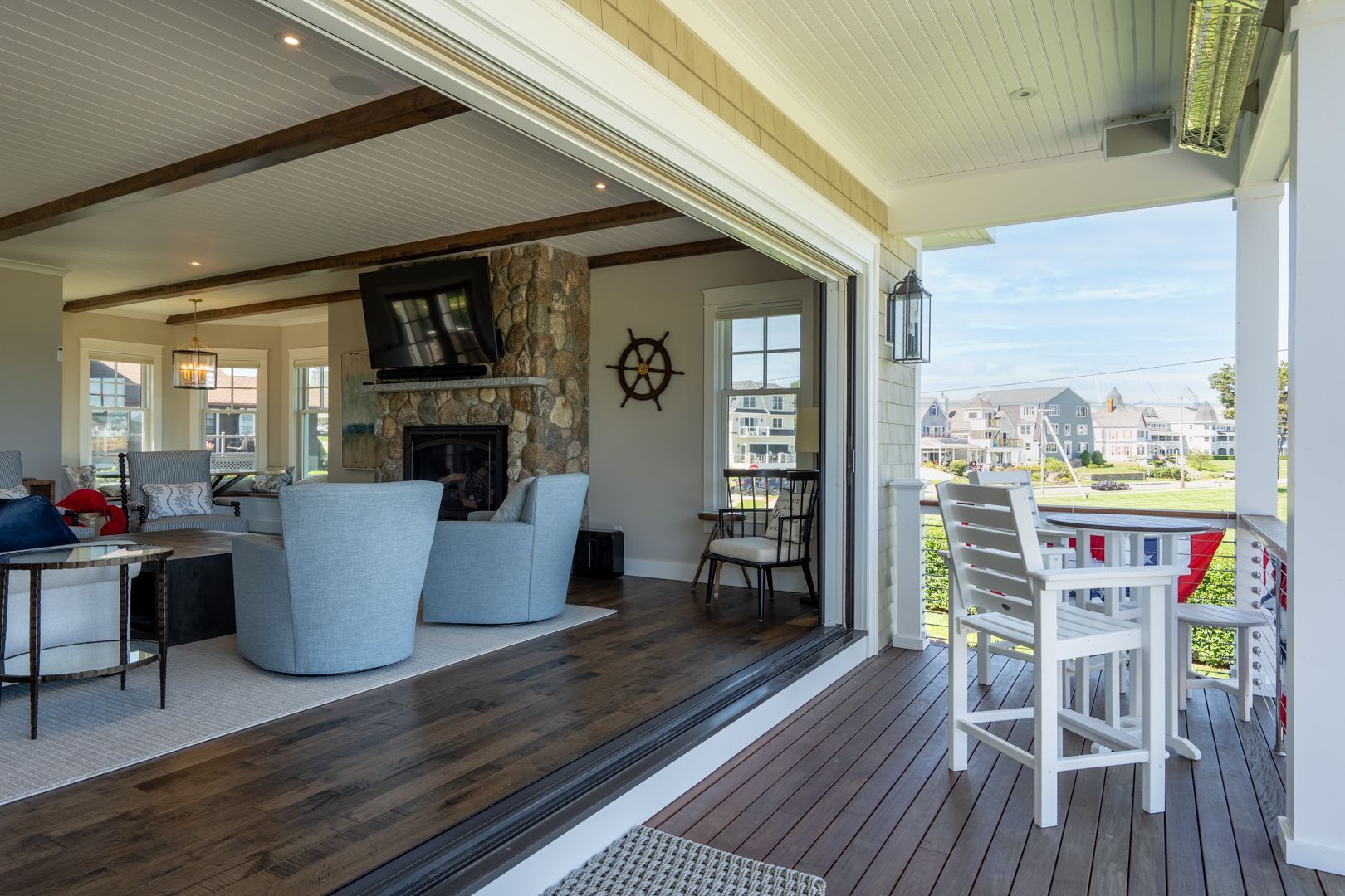 Covered deck with white chairs, wooden floor, and ocean-view opening to a bright living area