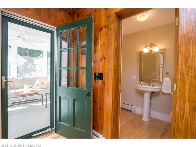Open front door beside a bathroom vanity, with a bright living room visible outside.
