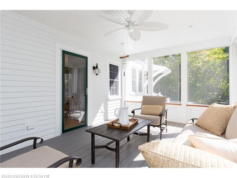 Bright screened porch with white shiplap walls, wicker seating, black table, and green door.