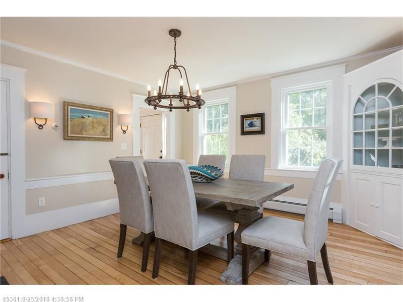 Bright dining room with a wooden table, upholstered chairs, chandelier, and large windows.