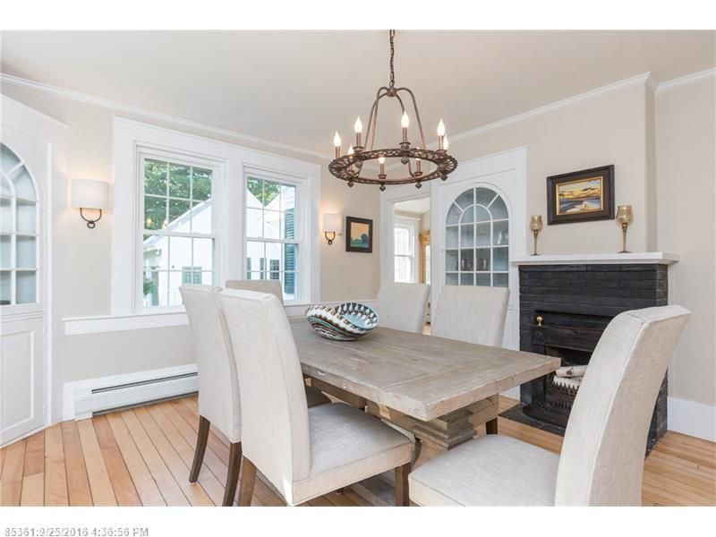 Bright dining room with rustic table, cream chairs, chandelier, fireplace, and large windows