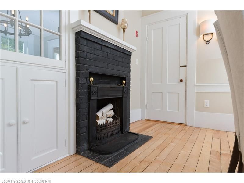 Bright hallway with black fireplace, white paneled walls, and light hardwood floors
