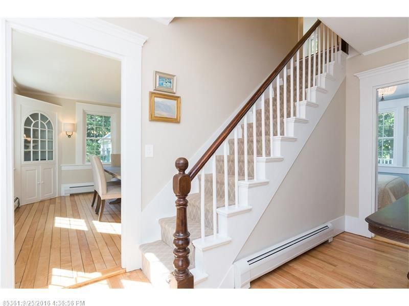 Bright foyer with wooden staircase, white walls, and sunlit hardwood floors leading to a dining room.