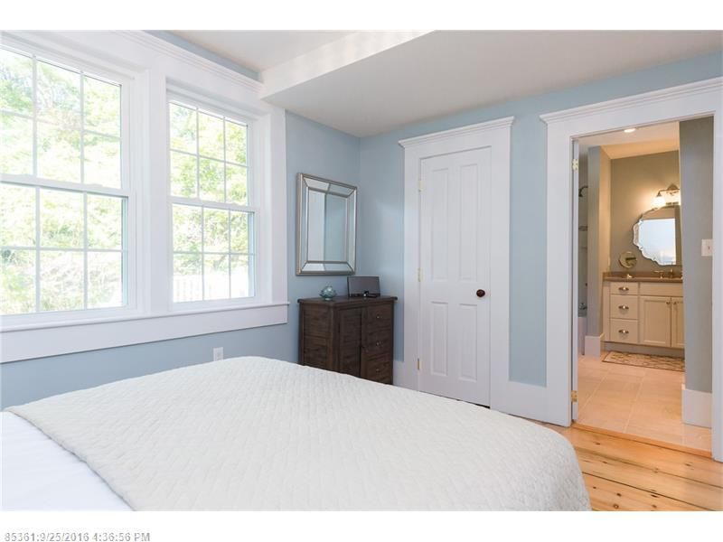 Bright bedroom with white trim, blue walls, large windows, dresser, and doorway to a bathroom.