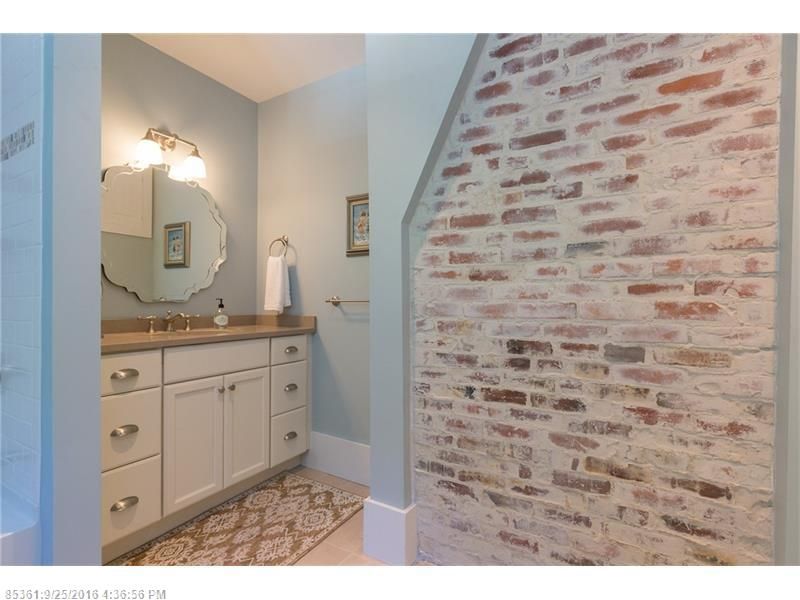 Small bathroom vanity with mirror, light wood countertop, and exposed brick accent wall.