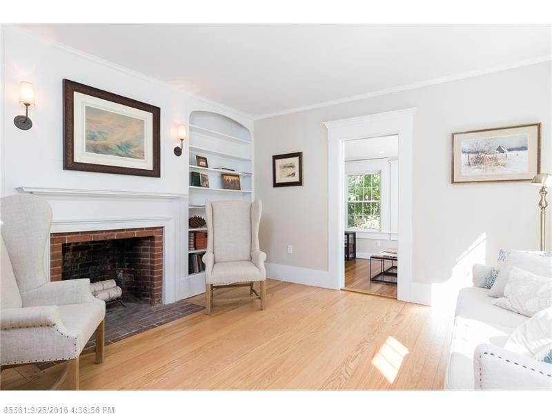 Bright living room with white walls, brick fireplace, armchair, and doorway to a sunlit dining area