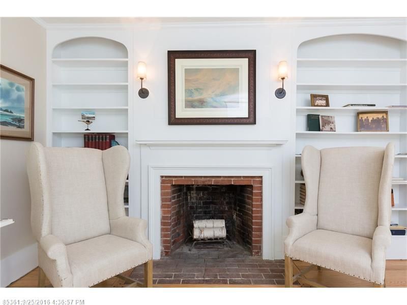 Elegant white living room with fireplace, built-in shelves, framed art, and two beige armchairs