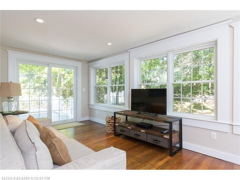 Bright living room with white sofa, TV stand, hardwood floors, and large windows overlooking greenery