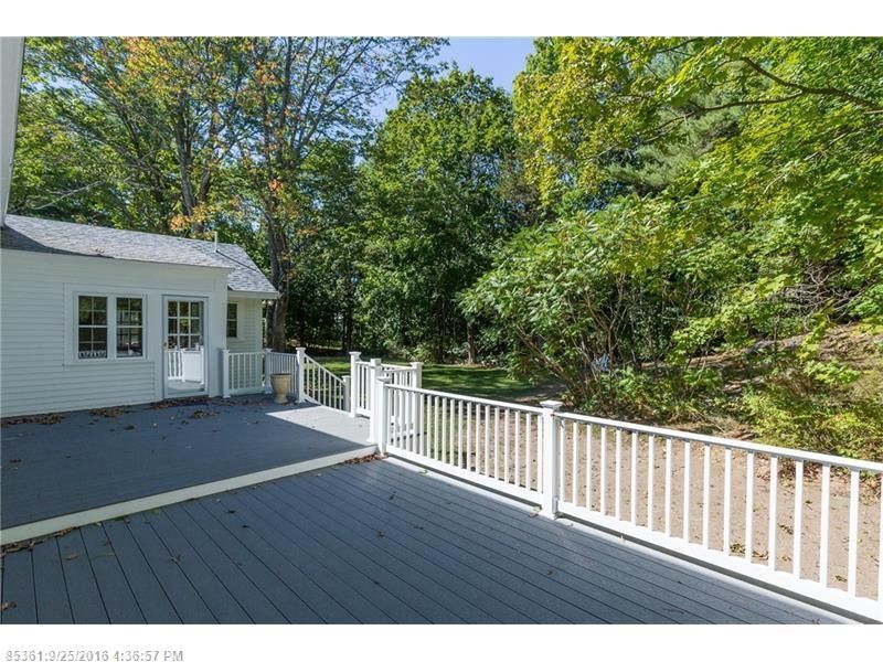 Deck beside a white house, overlooking a wooded yard on a sunny day