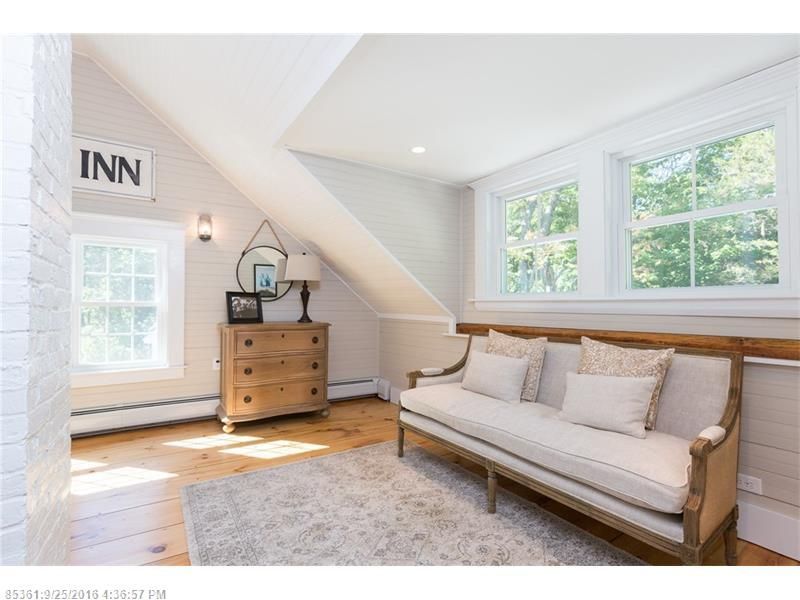 Bright attic bedroom with white walls, wood dresser, large windows, and a wooden daybed with neutral pillows.