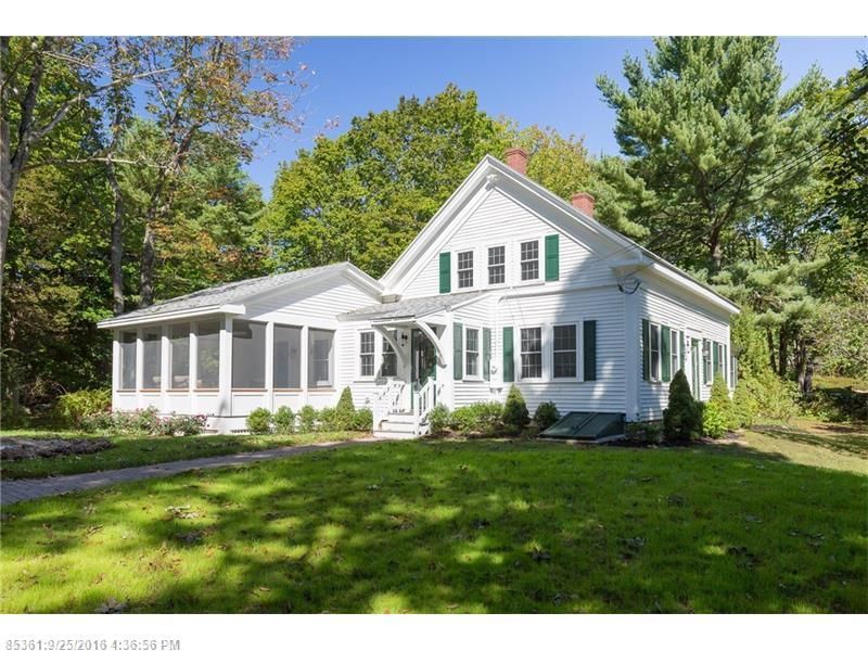 White house with green shutters and sunroom, set in a grassy yard with trees and blue sky.