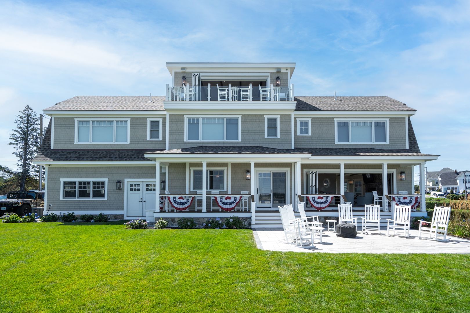 Large gray beach house with white porch chairs and an oceanfront lawn