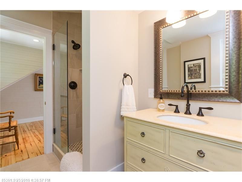 Bathroom with double vanity, mirror, and glass shower door leading to a wood-floored room
