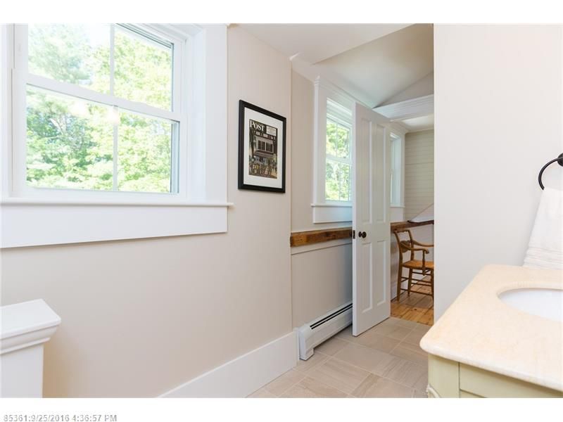 Bright hallway with white walls, windows, framed art, and a view into a dining room.