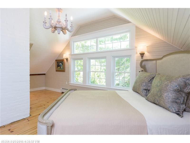 Bright attic bedroom with white bed, chandelier, and large windows under a sloped ceiling