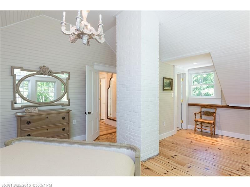 Bright bedroom with white walls, wood floors, ornate dresser, bed, and window seating nook