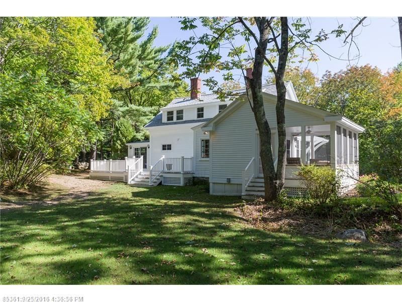 White house with screened porch and dormer windows in a leafy green yard under trees