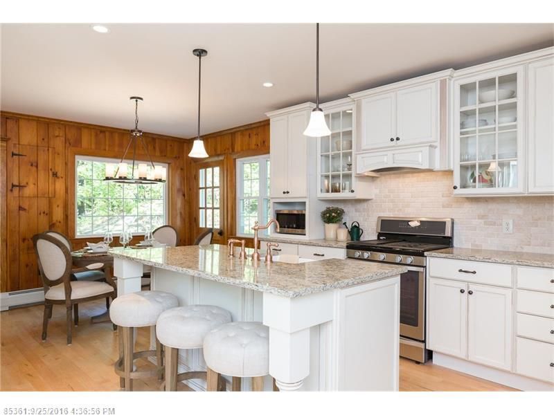 Bright kitchen with white cabinets, granite island, barstools, wood-paneled wall, and hanging pendant lights