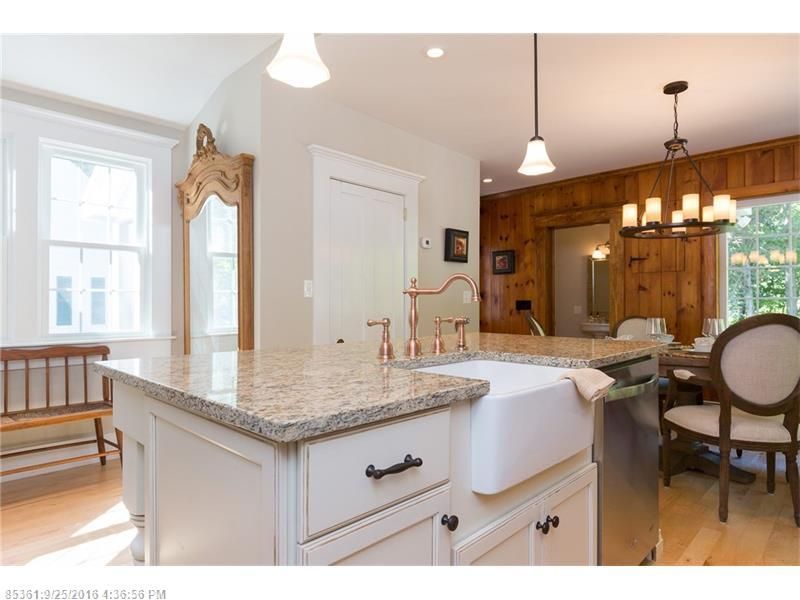 Bright kitchen with granite island, white cabinets, wood-paneled dining area, and large windows.